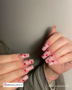 Cute Christmas Acrylic Nails With Hearts And Stones In Front Of White Wall