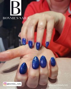 Glittery Royal Blue Almond Acrylic Nails Over White Surface