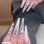 Glittery Stiletto Summer Acrylic Nail Designs With Marble Design And Rhinestones Over White Surface