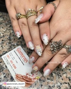 Glittery White Almond Acrylic Nails With Gems And Butterfly Over Marble Surface