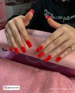 Glossy Square Blood Red Acrylic Nails On Pink Surface