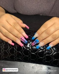 Gorgeous Pink And Blue Acrylic Nails With Inscriptions And Stones Over Black Surface