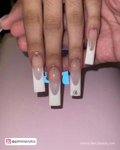 Long French Tip White Acrylic Nails With Stones And Inscription Over Light Pink Surface