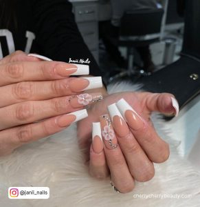 Long Nude Acrylic Nails With White Flowers And Diamonds On Ring Finger