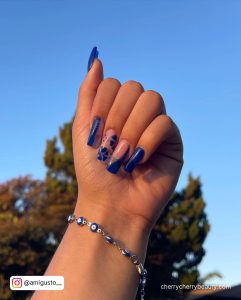 Royal Blue Long Acrylic Nails With Flowers And The Sky In The Background