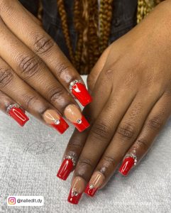 Short Square Red Acrylic Nails With Gems Over White Surface